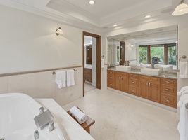 Spa-style bathroom with soaking tub, dual vanities, and tropical garden views through warm wood-framed windows.
