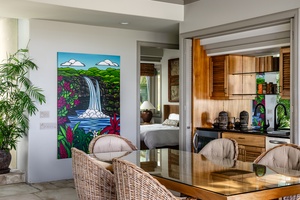 Bright dining area with tropical artwork and a view into the cozy bedroom.