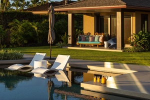 Tropical luxury estate with pool ledge loungers, verdant gardens, and covered lanai in golden sunset light.