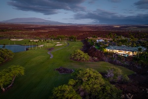 Aerial view of a scenic golf course at dusk, with lush greenery and a luxurious home.