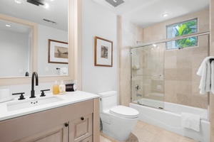 Your elegant bathroom features a glass-enclosed tub, modern fixtures, and soft natural light from the window above.
