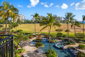 Stunning resort pool surrounded by swaying palms and golf course views under tropical blue skies.