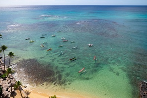 Aerial view showcasing pristine turquoise waters dotted with colorful boats along a palm-fringed coastline.