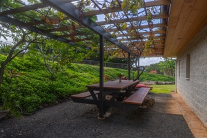 Outdoor picnic area with a rustic wooden table and bench seating for 8, shaded by a charming pergola.