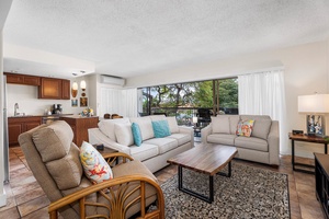 Relax in your spacious living area with comfortable seating, modern kitchen, and lanai overlooking lush greenery.