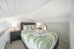 A queen bed dressed in island greens, nightstand and lamp ready for late reading.