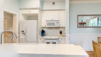 The bright kitchen features many amenities including a fridge, oven, extended counter-tops and high ceilings.