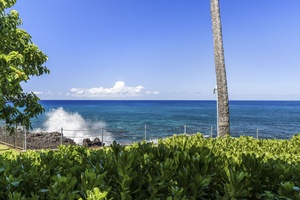 Stunning oceanfront setting with tropical palms and dramatic waves crashing against volcanic rocks under brilliant blue skies.