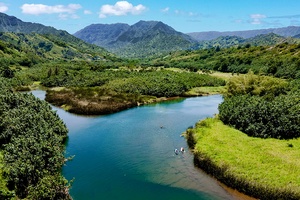 Tranquil Hanalei River surrounded by lush greenery and rolling mountains, ideal for kayaking or a peaceful stroll.