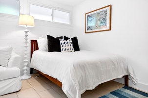 Sink into crisp white linens with plush pillows in your serene bedroom, where soft lamplight and coastal artwork create perfect tranquility.