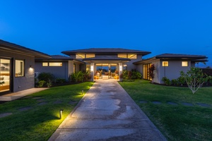 Modern luxury villa entrance illuminated against the evening sky, featuring contemporary architecture and manicured tropical landscaping.