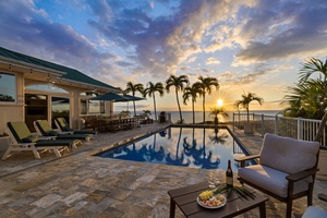 Tropical sunset paints the sky as palm trees frame this oceanfront pool deck, complete with comfortable seating and refreshments awaiting your arrival.