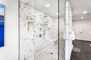Frameless glass walk-in shower with rain head, handheld sprayer, and sleek design.