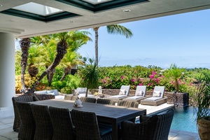 Outdoor dining area with comfortable seating and lounge chairs, surrounded by tropical landscaping