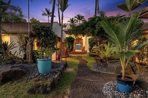 Hahalua Bay Villa entrance features lush landscaping and warm island architecture beneath a stunning twilight sky.