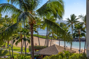 Tropical paradise view featuring palm-fringed beach, protected swimming lagoon, and lush grounds with mountain backdrop.
