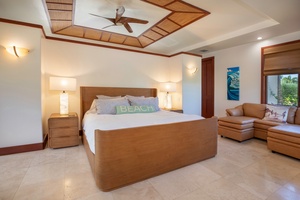 Primary bedroom with king bed, cozy seating nook, and warm island-inspired finishes.