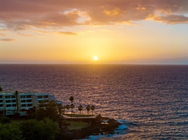 Golden sunset paints the sky above oceanfront property with dramatic clouds and shimmering waters stretching to the horizon.