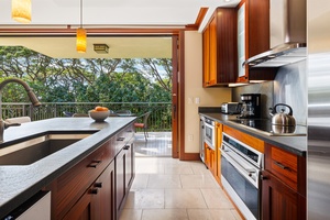 Your elegant kitchen opens onto a private balcony with lush treetop views, blending modern appliances and rich wood cabinetry for a seamless indoor-outdoor cooking experience.