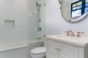 Guest bath with soaking tub, shower combo, and round mirror vanity.