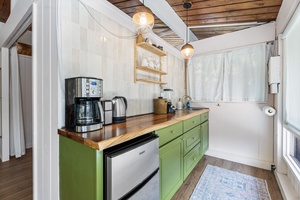 Step into your charming cottage kitchenette with vibrant green cabinets, warm wood countertops, and all the essentials for your perfect getaway meals.