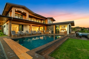 Modern luxury villa with pool and outdoor terrace surrounded by manicured lawns at sunset.