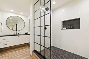 This modern ensuite bathroom offers a luxurious walk-in shower with sleek black accents, a stylish glass partition, and a convenient built-in shelf for toiletries