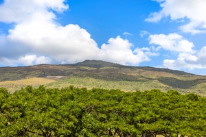 Dramatic mountain landscape with rolling hills and lush green vegetation under a brilliant blue sky with white clouds.