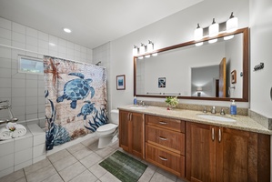 Ensuite bath featuring dual sinks, granite counters, and a shower/tub combo accented by local art for a touch of island charm.