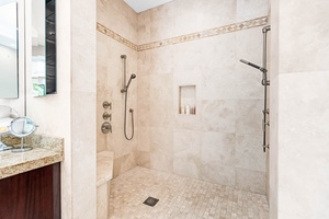 Stone-tiled walk-in shower with dual showerheads and bench seating.