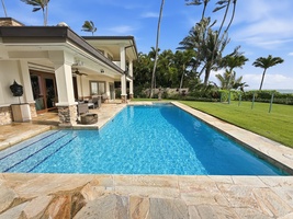 Stunning oceanfront estate with pristine pool surrounded by swaying palms and manicured lawns under tropical blue skies.