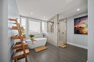 Primary bathroom with a luxurious soaking tub, custom glass shower, and serene greenery views.