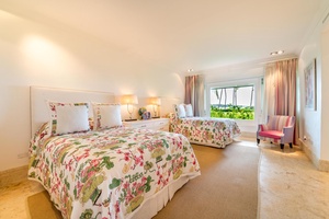 This guest bedroom offers two plush beds, cheerful floral decor, and a serene garden view.