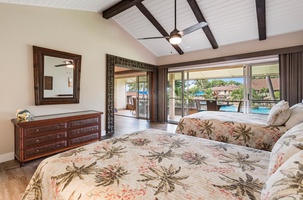 This airy and inviting bedroom features vaulted ceilings with exposed beams and large sliding doors that open onto the lanai, allowing for an easy flow between indoor and outdoor spaces