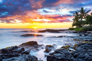 Vivid Hawaiian sunset with dramatic skies over lava rock shoreline.