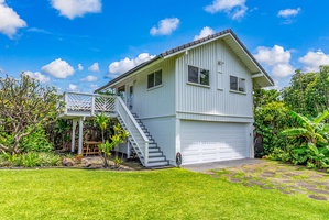 Elevated home with tropical landscaping, featuring a private garage and surrounded by lush greenery under clear blue skies.