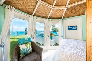 Oceanfront bedroom with a woven bamboo ceiling and views framed by swaying palms.