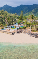 A front-facing view of the home set directly on the sand, offering private beach access, turquoise snorkeling waters, and a dramatic backdrop of Sacred Falls and Jurassic Valley sea cliffs.