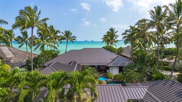 Roofline silhouette against tropical landscaping with glimpses of Kailua Bay beyond.