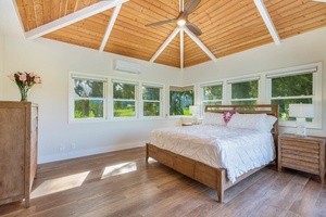 Spacious primary suite at Pohaku Villa with vaulted ceilings, king bed, and wraparound windows with tropical views.