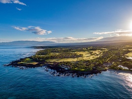 Spectacular aerial view showcasing the dramatic coastline where lush golf fairways meet volcanic shores and crystal-clear Pacific waters.