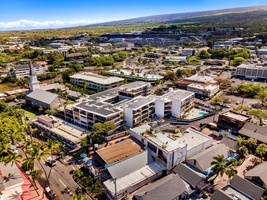 Aerial view of a charming tropical town with mix of modern buildings, local shops, and lush greenery beneath blue skies.