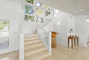A central staircase with glass railings and soaring windows connects the estate’s two levels with style and natural light.