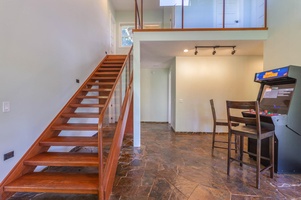 The central stairway at Pohaku Villa leads to upper bedrooms, blending stone floors and warm wood finishes.