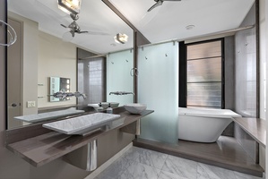 A sleek and modern ensuite bathroom featuring a large soaking tub, dual vanities, a frosted glass shower, and elegant finishes.