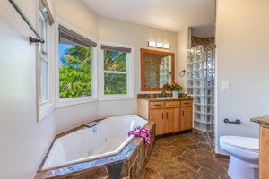 Pohaku Villa ensuite with soaking tub set against windows, offering a serene garden outlook.
