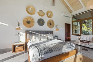 Retreat in the primary bedroom featuring a cozy sitting area, a unique collection of wall mirrors, and plush bed.