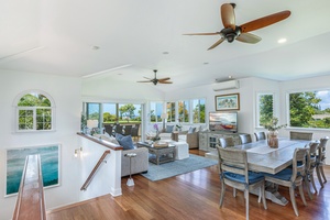 Spacious upstairs lounge and dining area with wood floors, ceiling fans, and expansive windows framing lush views.
