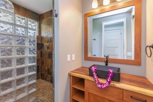 Modern ensuite bath at Pohaku Villa with stone-tiled walk-in shower and bright vanity space.