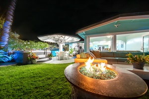 After dark, the fire pit glows on the lawn while the house lights up behind.